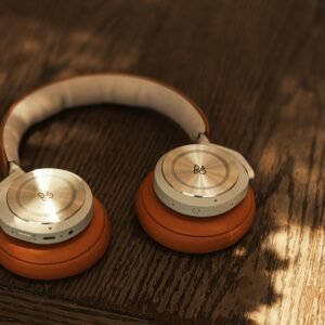 Stylish wireless headphones with orange cushions on a wooden surface, lit by natural light.