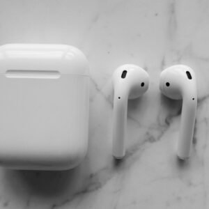 Close-up of wireless earbuds and charging case on a white marble background with soft lighting.